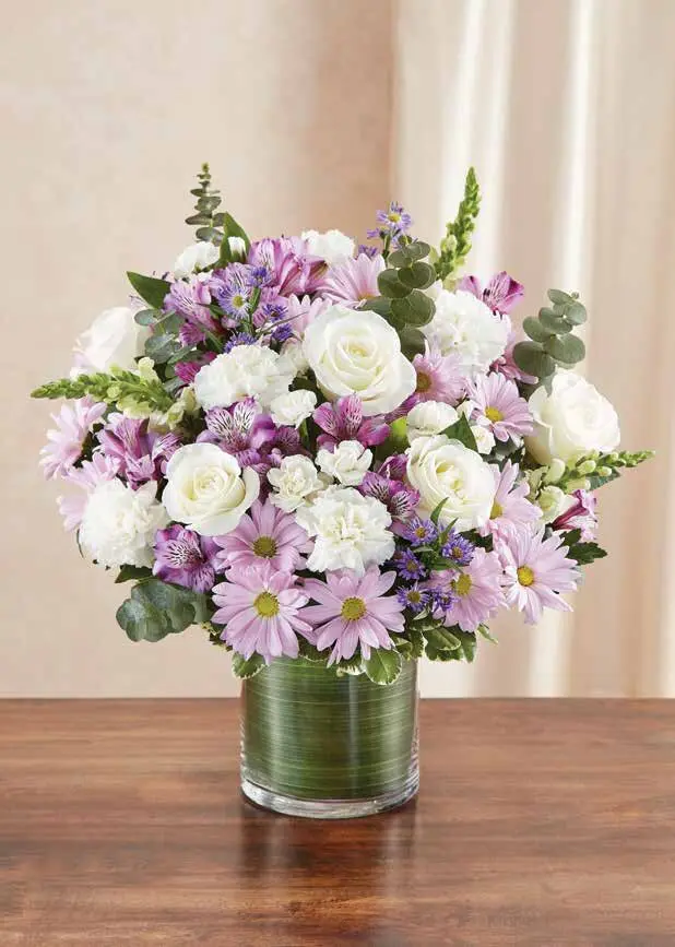 Lavender, pink and white roses and daisies in a leaf-lined glass cylinder