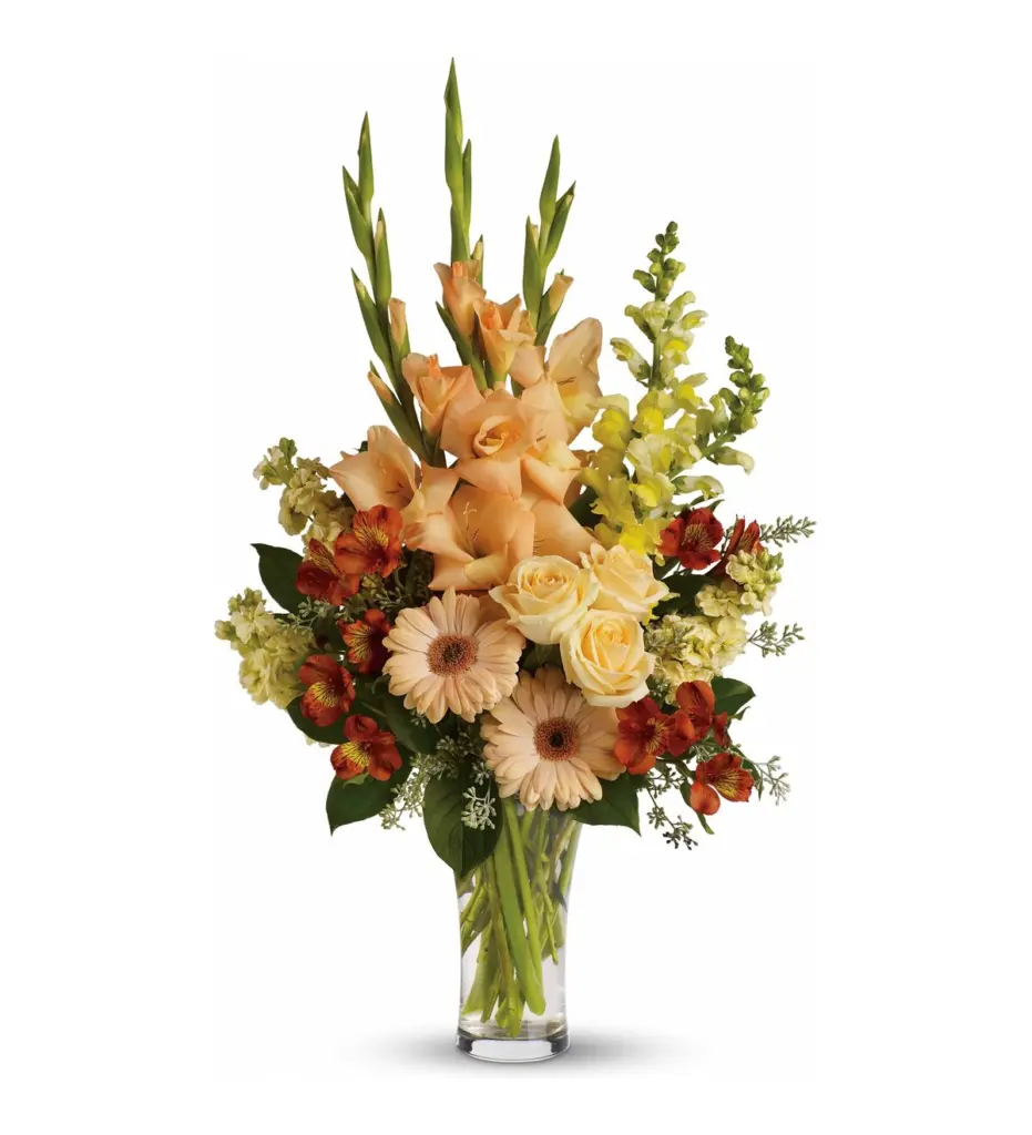 Peach gladiolus, cream roses and peach gerberas in a clear glass vase