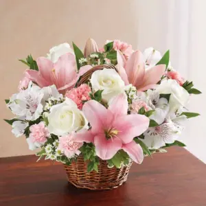 Pink lilies and white roses in a small woven handled basket on a table