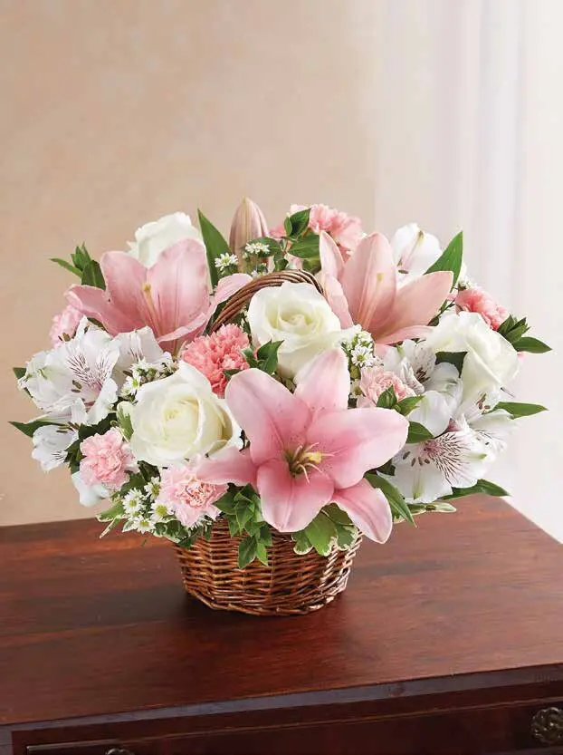 Pink lilies and white roses in a small woven handled basket on a table