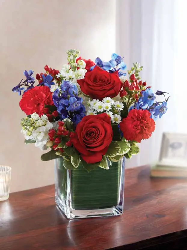 Red roses, carnations and blue delphinium in a leaf-lined glass cube vase