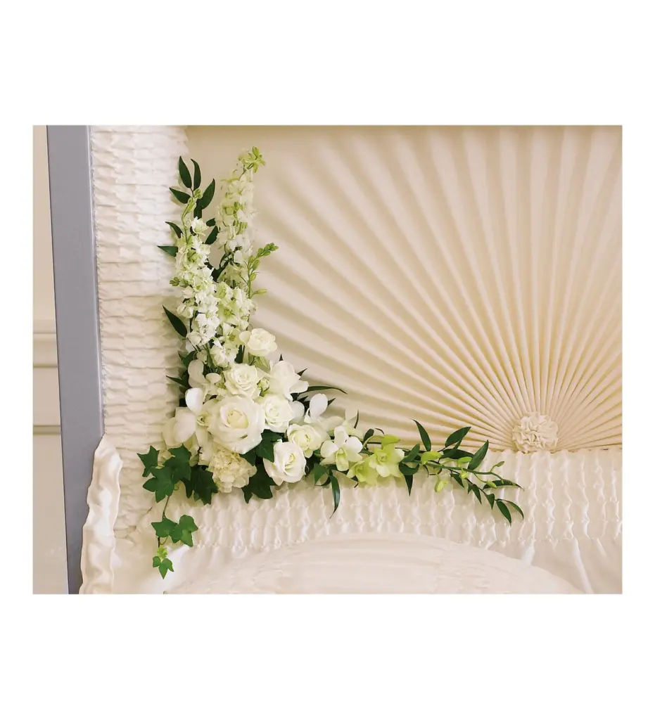 White roses, orchids and larkspur corner piece inside an open casket lid