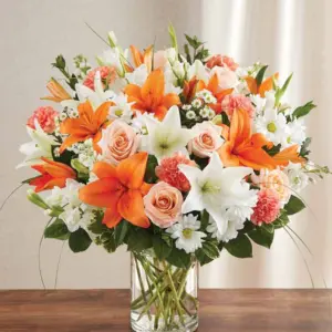 Orange and white lilies with peach roses in a clear glass cylinder vase