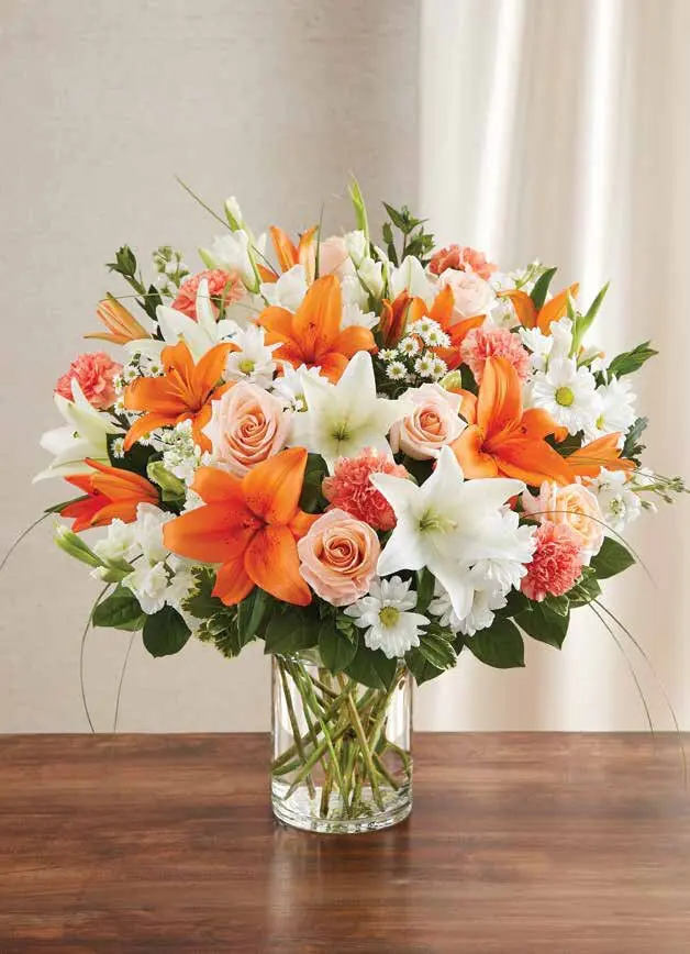 Orange and white lilies with peach roses in a clear glass cylinder vase