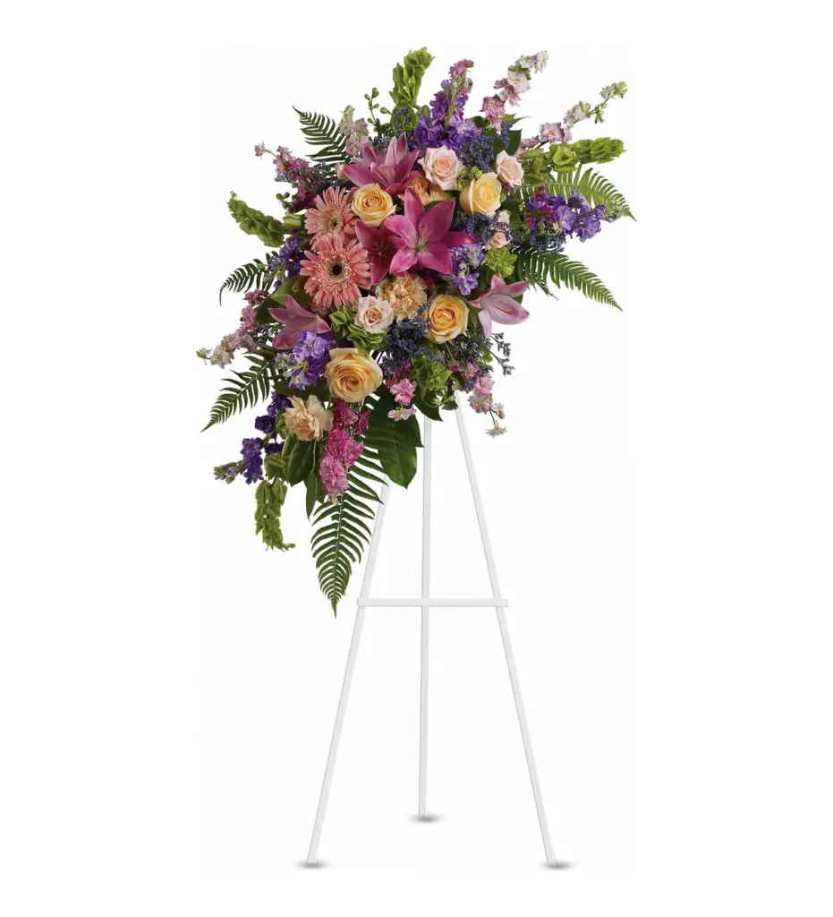 Pastel standing spray of pink lilies, gerberas, peach roses and purple stock on easel