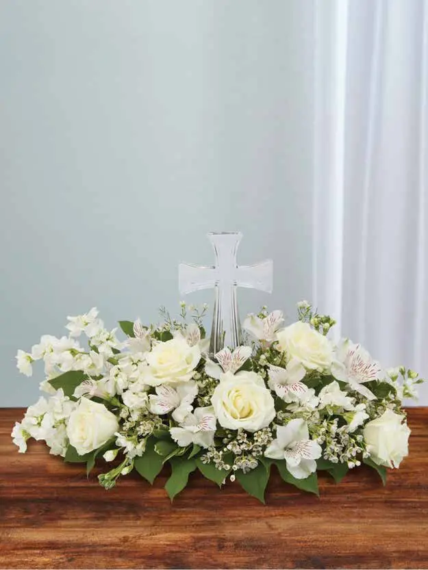 White roses and alstroemeria arranged low around a clear glass cross