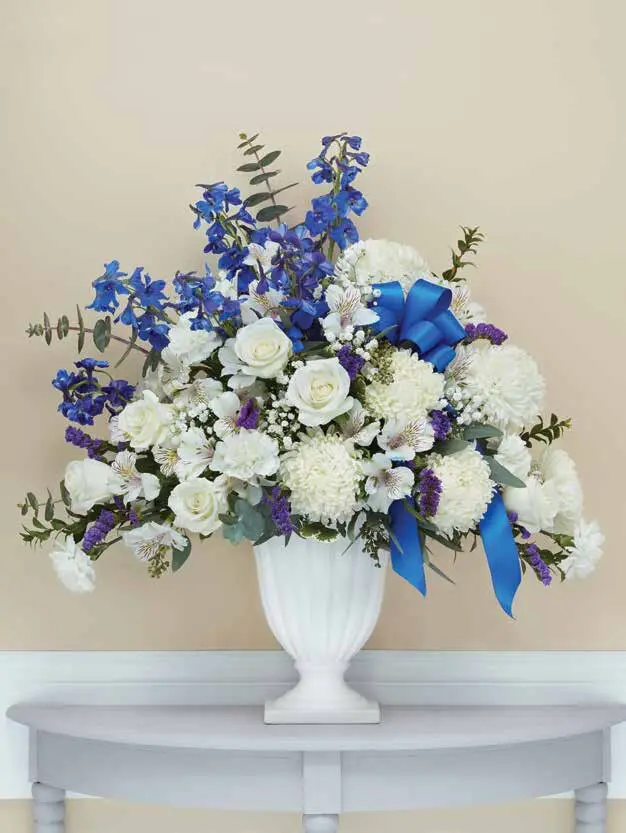 Blue delphinium and white roses in a white fluted urn with blue bow