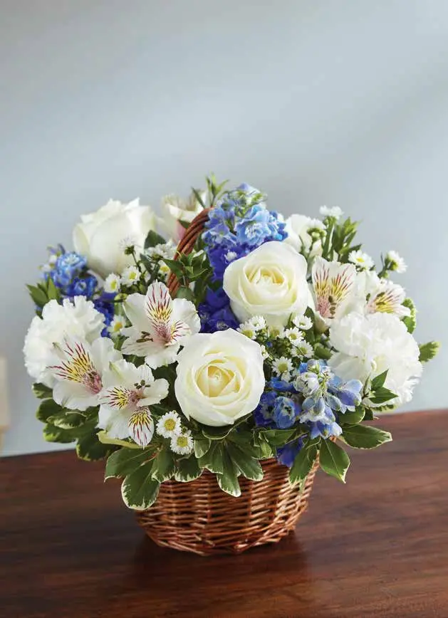 White roses and blue delphinium in a small woven handled basket