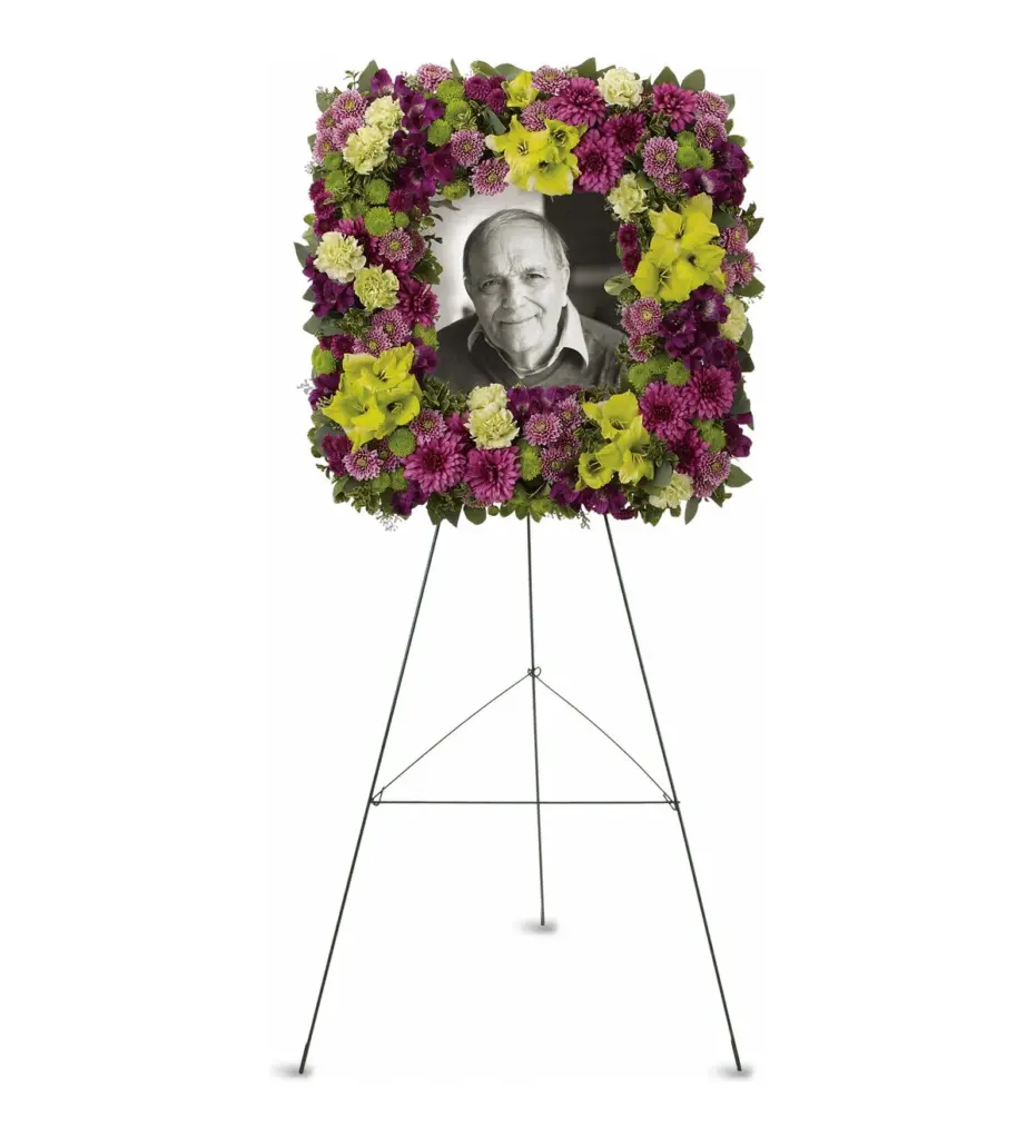 Square frame of purple mums and green gladiolus around a photo on easel