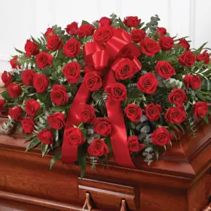 Red rose half casket spray with red satin bow on a wooden casket