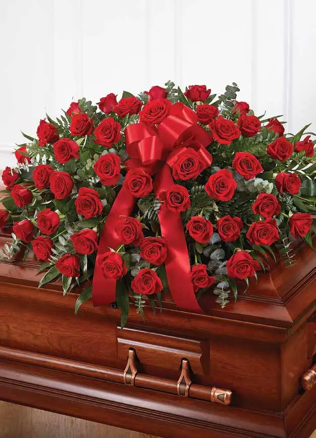 Red rose half casket spray with red satin bow on a wooden casket
