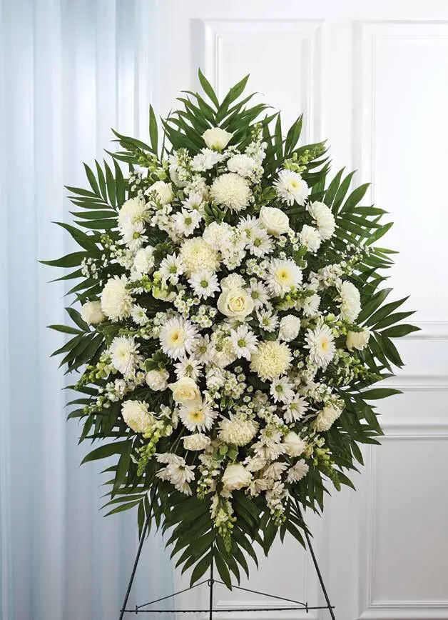 White standing spray of mums, daisies and roses framed with palm leaves on an easel