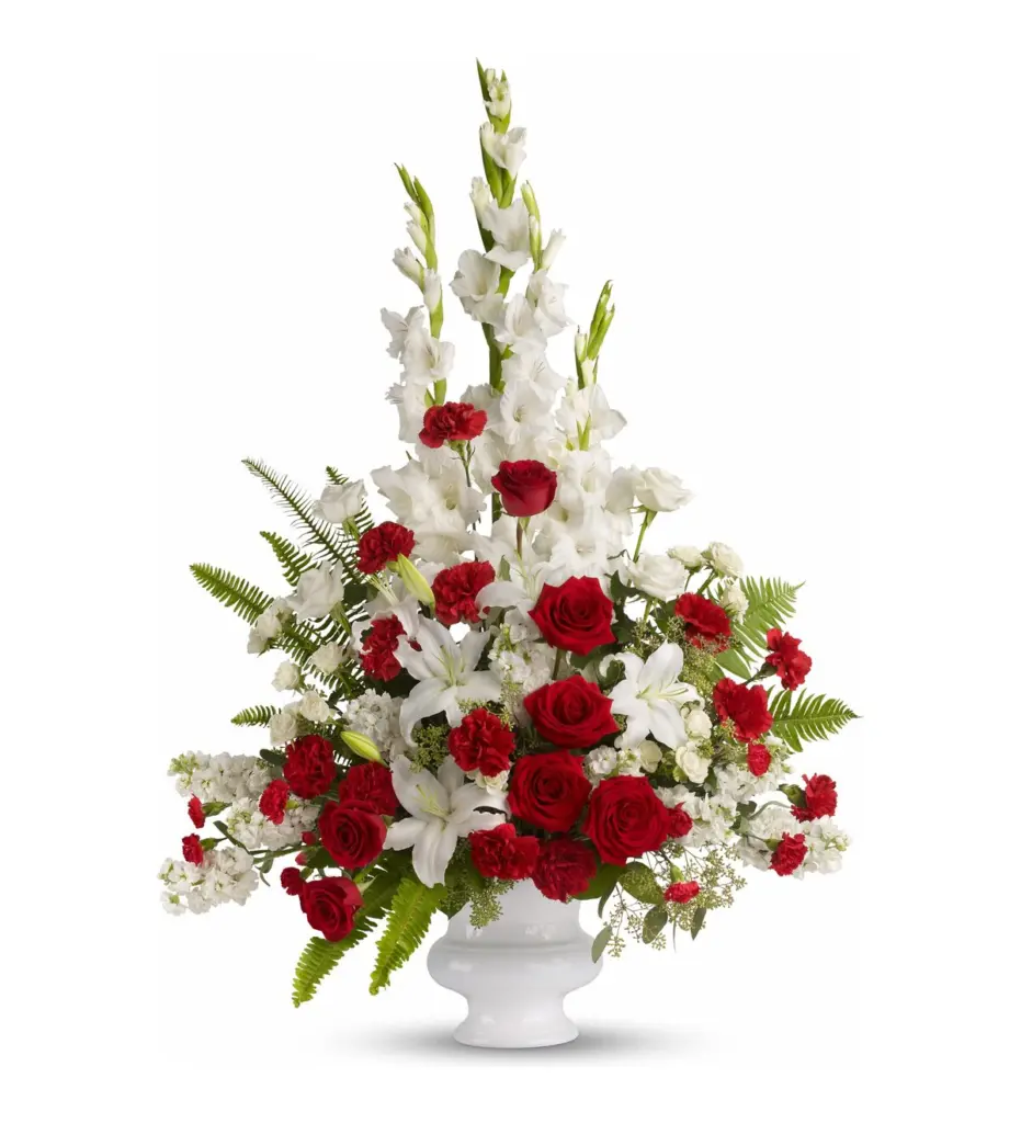 Tall red and white arrangement of roses and gladiolus in a white pedestal urn