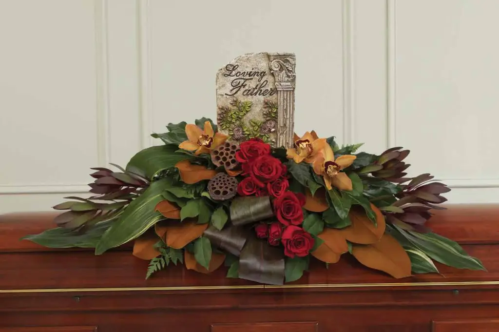 Red roses and orange orchids around a Loving Father plaque on a casket