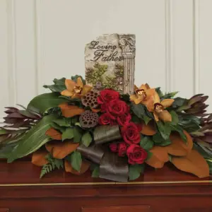 Red roses and orange orchids around a Loving Father plaque on a casket