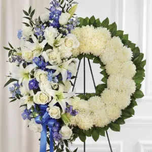 White mum wreath with white roses, lilies and blue delphinium on an easel