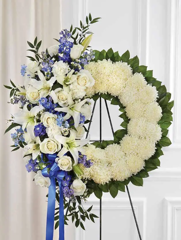 White mum wreath with white roses, lilies and blue delphinium on an easel