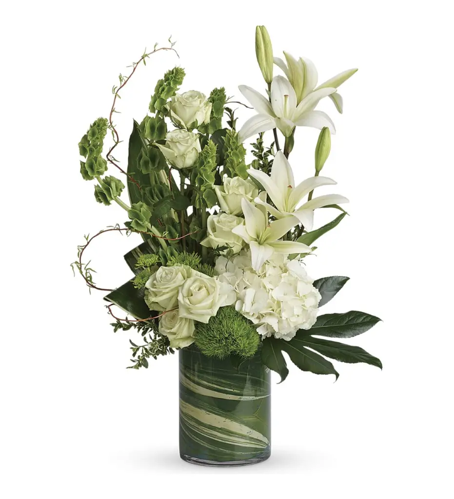 White lilies, roses and hydrangea with bells of Ireland in a leaf-lined glass cylinder