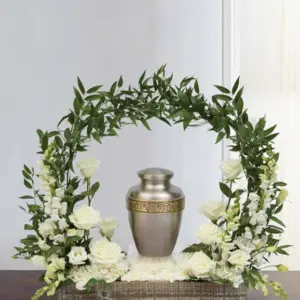 White roses and snapdragons in a wooden box under a greenery arch framing an urn
