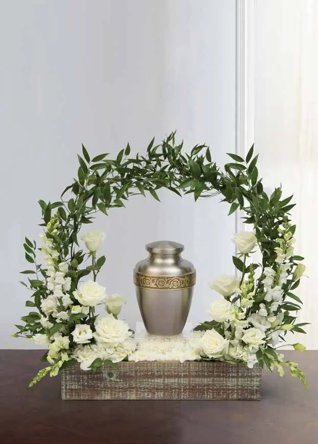 White roses and snapdragons in a wooden box under a greenery arch framing an urn