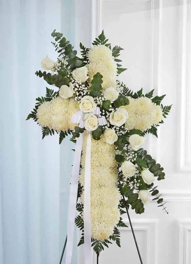 White standing cross of mums and roses with a white ribbon on an easel