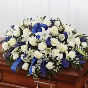 Blue and white half casket spray with a blue bow on a wooden casket
