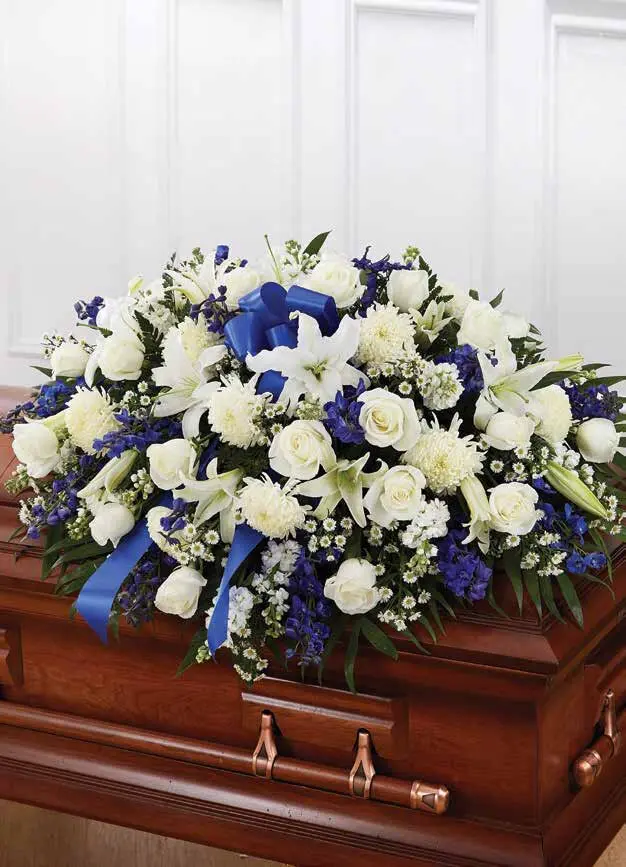 Blue and white half casket spray with a blue bow on a wooden casket