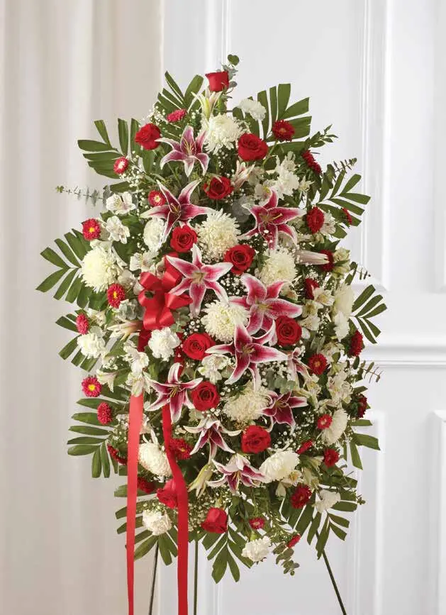 Red roses, pink lilies and white mums in an oval standing spray on an easel