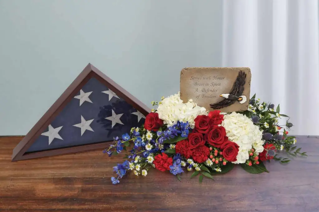 Red roses and white hydrangea with an eagle plaque beside a folded flag case