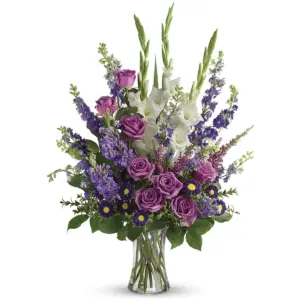 Purple and white flowers in a clear glass vase with roses and gladiolus
