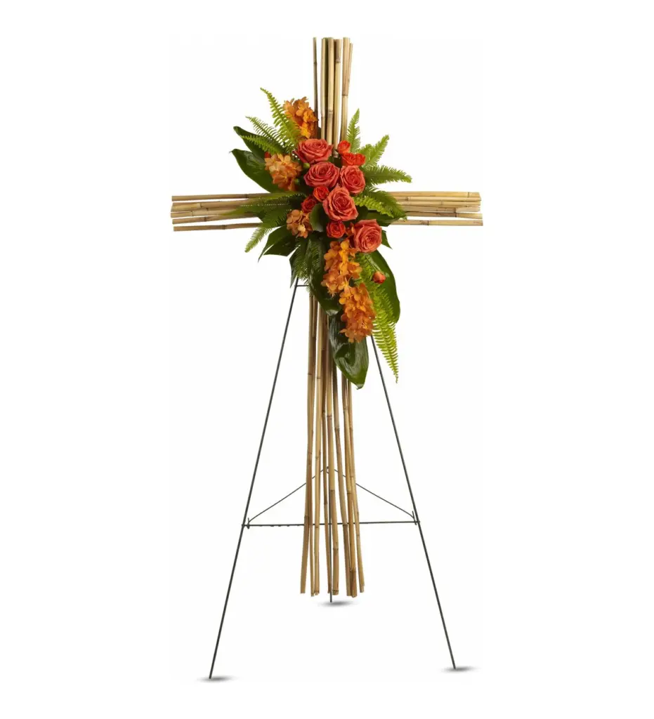 Bamboo cane cross on easel with orange roses, orchids and fern cascade