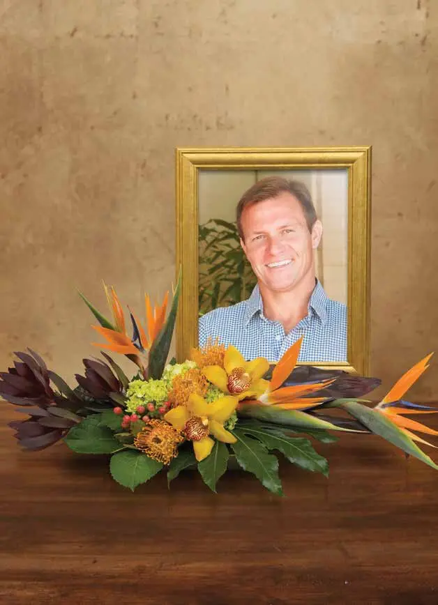 Birds of paradise and orchids in a low design before a gold photo frame