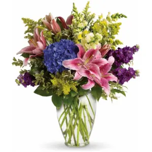 Pink lilies, blue hydrangea and purple stock in a clear glass vase