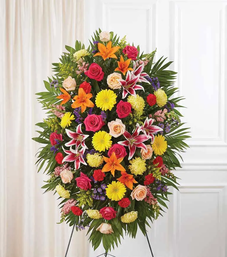 Oval standing spray of lilies, gerbera daisies, roses and carnations framed with palm