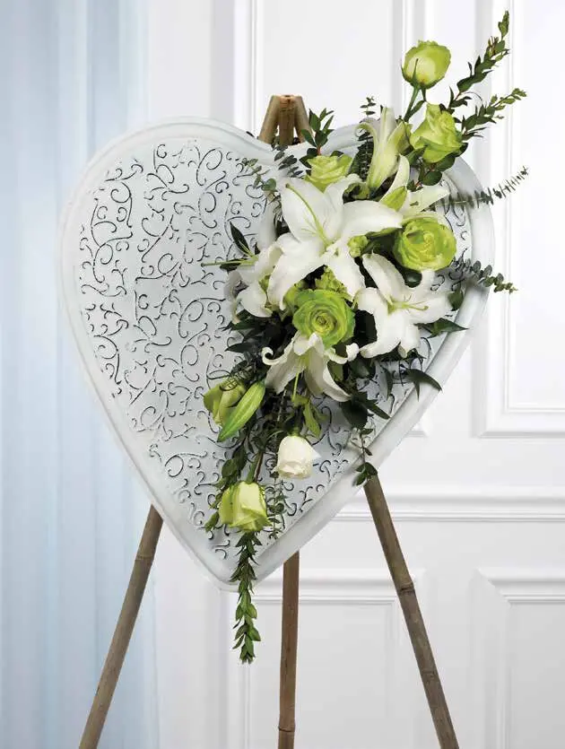 White scrolled heart on wooden easel with a cascade of white lilies and green roses