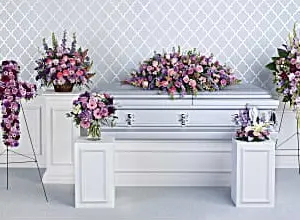 Funeral room with lavender casket spray, floral cross, standing spray and table pieces