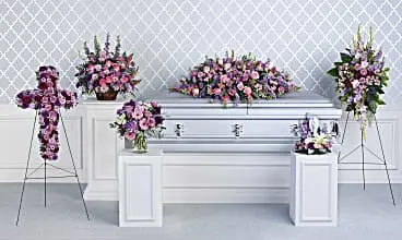 Funeral room with lavender casket spray, floral cross, standing spray and table pieces