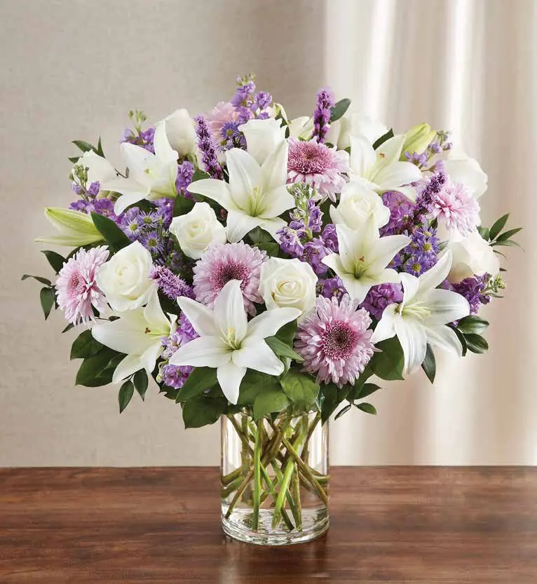 White lilies, roses and pink mums with purple stock in a clear glass cylinder