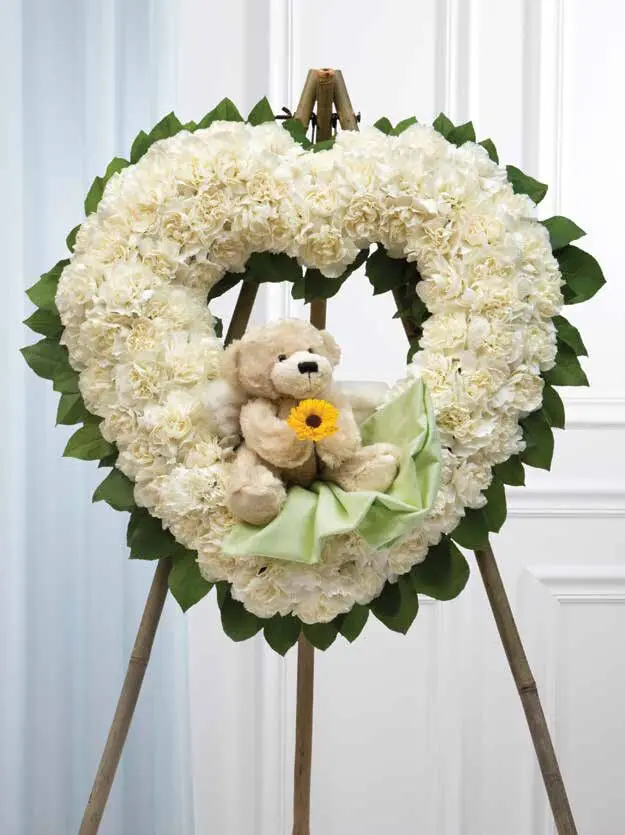 White carnation heart on a wooden easel with a teddy bear holding a yellow daisy