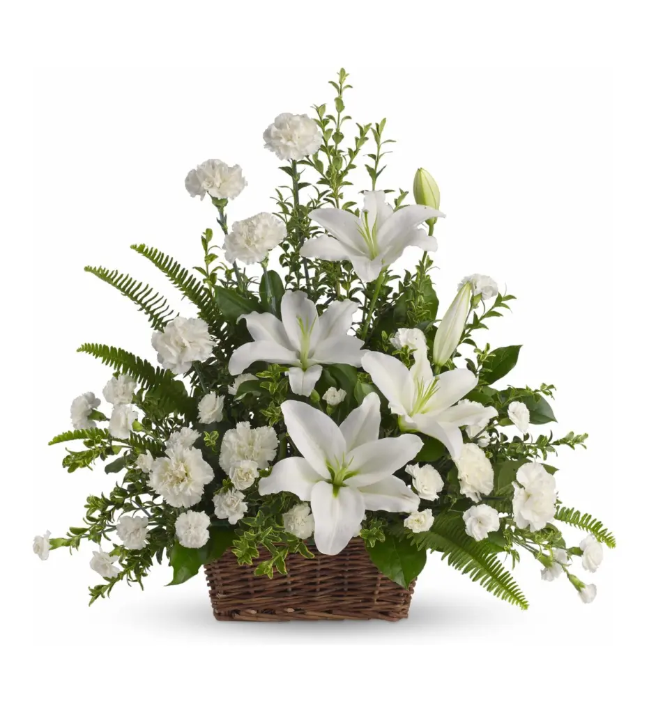 White lilies and carnations fanned in a brown wicker basket with fern