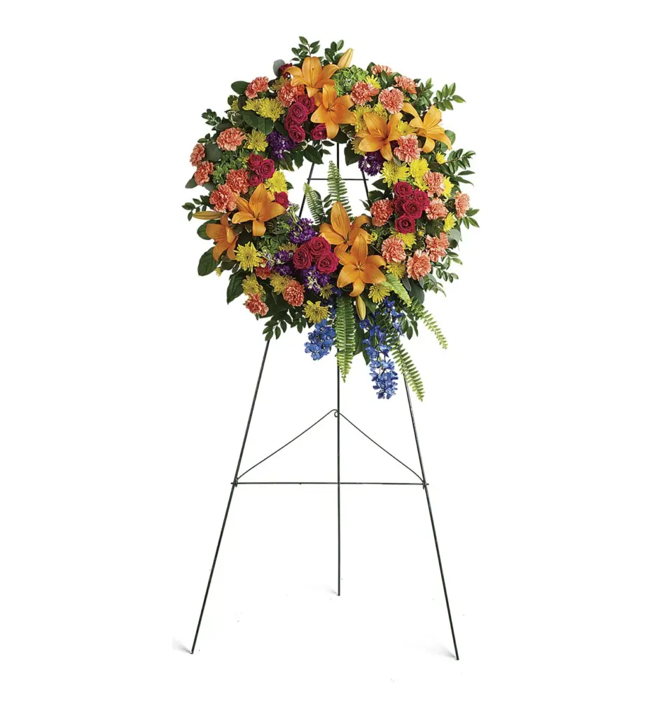 Round wreath of orange lilies, carnations and pink roses on a wire easel