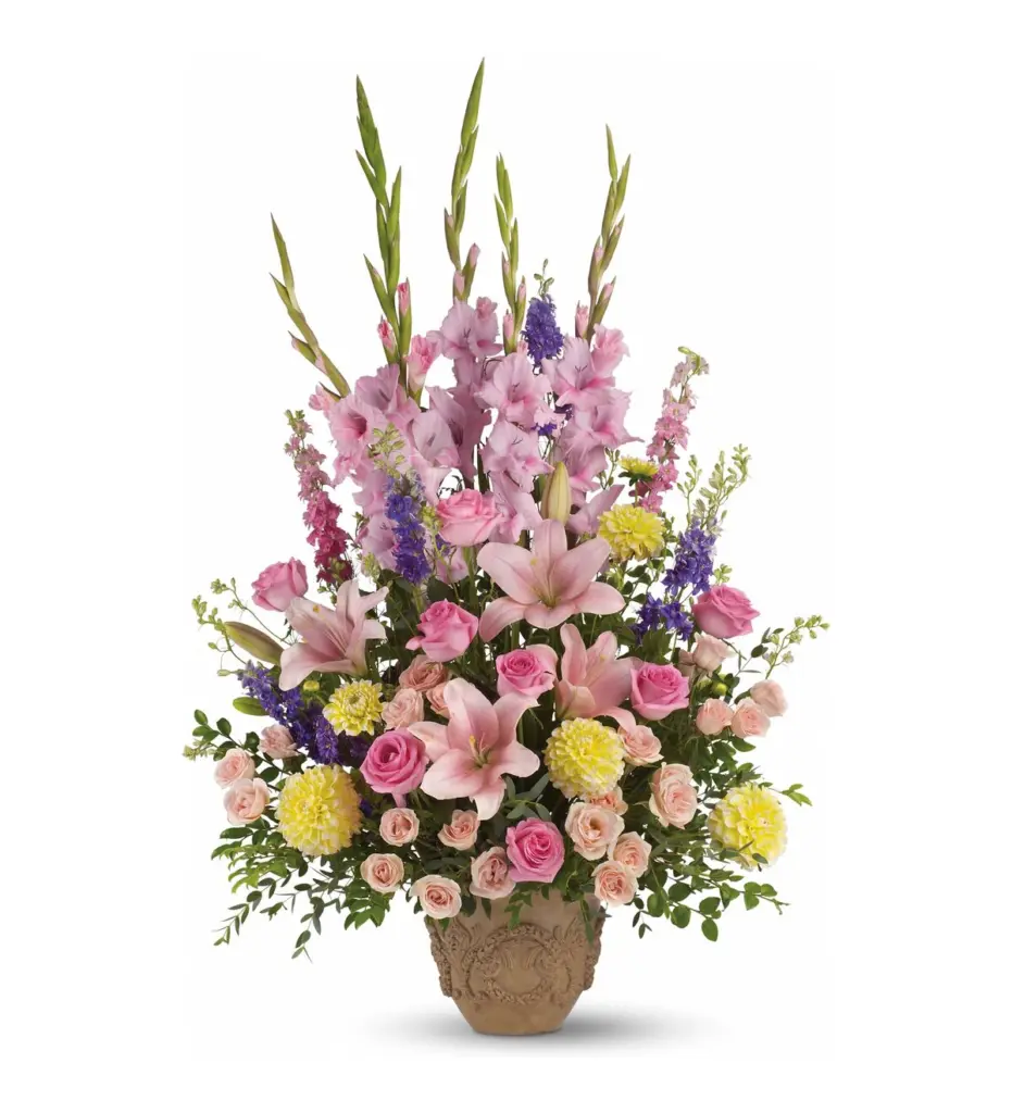 Tall pastel arrangement of pink gladiolus, lilies and roses in a carved tan urn