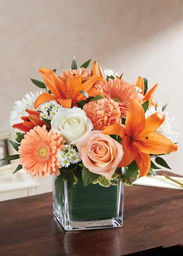 Orange lilies, peach gerberas and roses in a leaf-lined glass cube