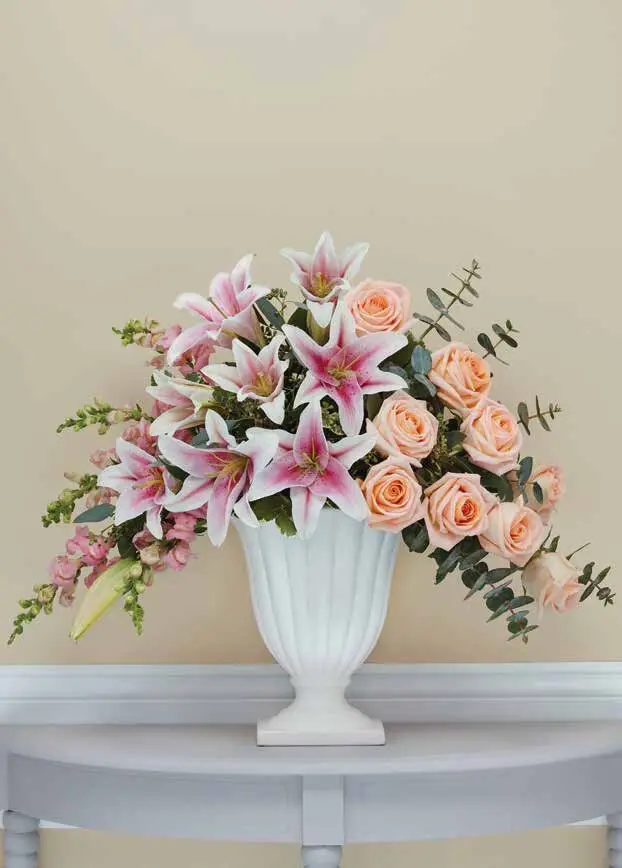 Pink lilies, peach roses and snapdragons in a white fluted pedestal urn