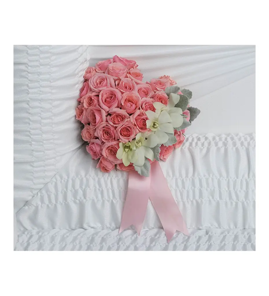 Heart of pink roses with white orchids and pink ribbon on white casket lining