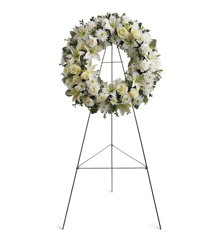 Round white wreath of lilies, roses and carnations on a green wire easel
