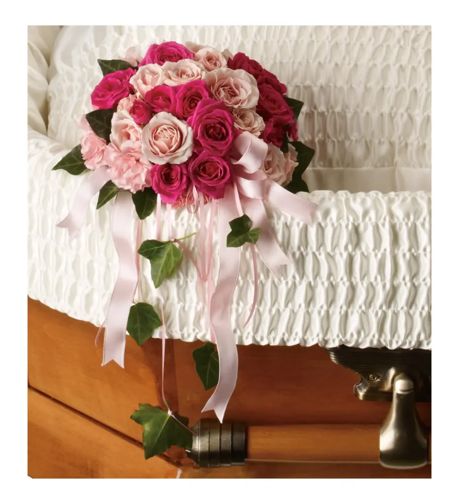 Small bouquet of pink spray roses with pink ribbons inside an open casket