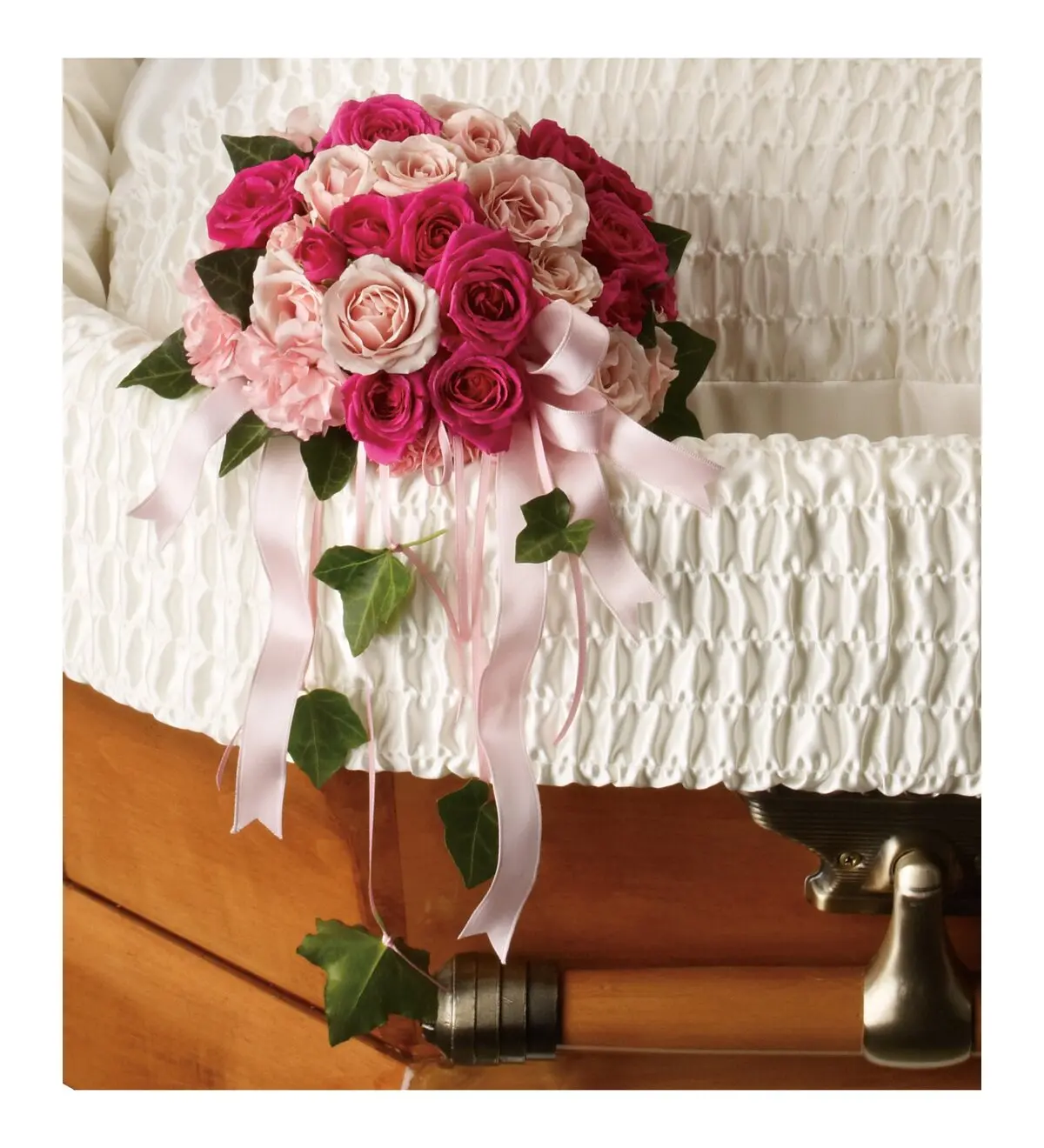 Small bouquet of pink spray roses with pink ribbons inside an open casket