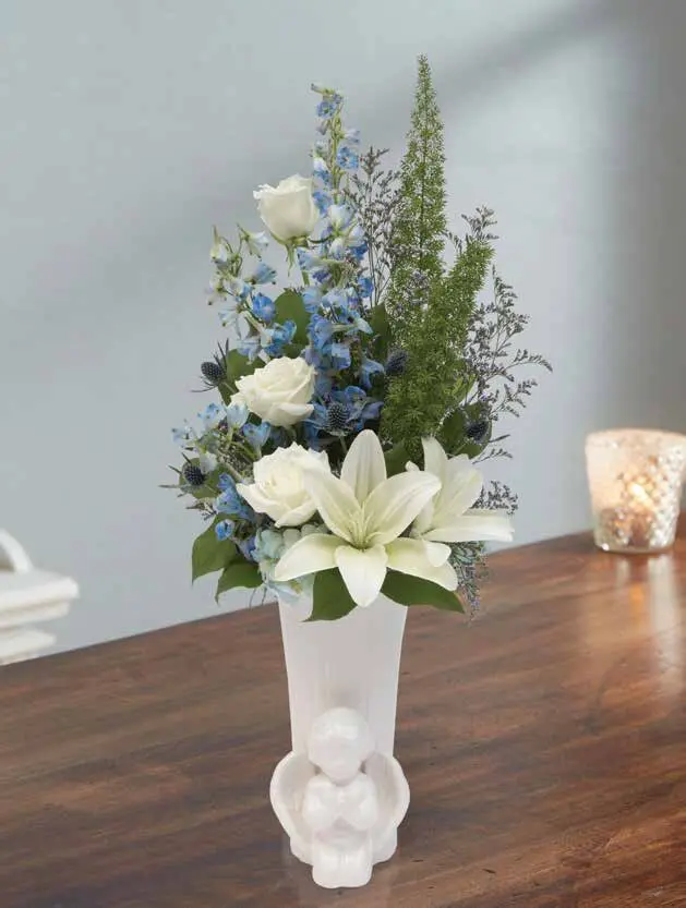 White roses, lilies and blue delphinium in a white cherub vase