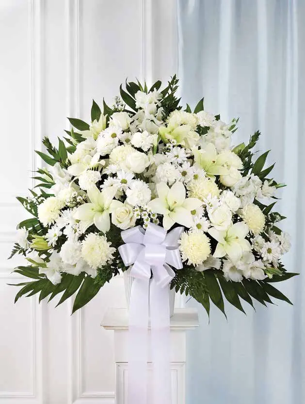 White floor basket of lilies, roses and carnations with a white bow on a pedestal
